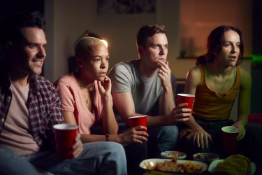 group-of-friends-with-drinks-sitting-on-sofa-at-home-watching-horror-movie-together.jpg